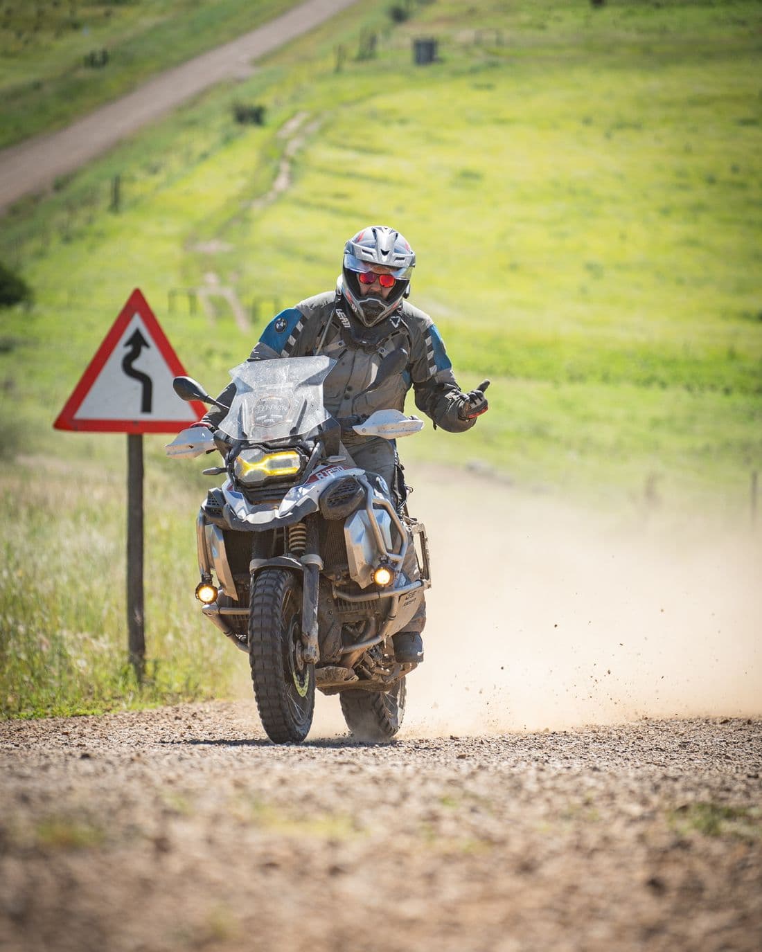 A mud-spattered BMW GS riding a gravel road, dust kicking up behind the rear wheel